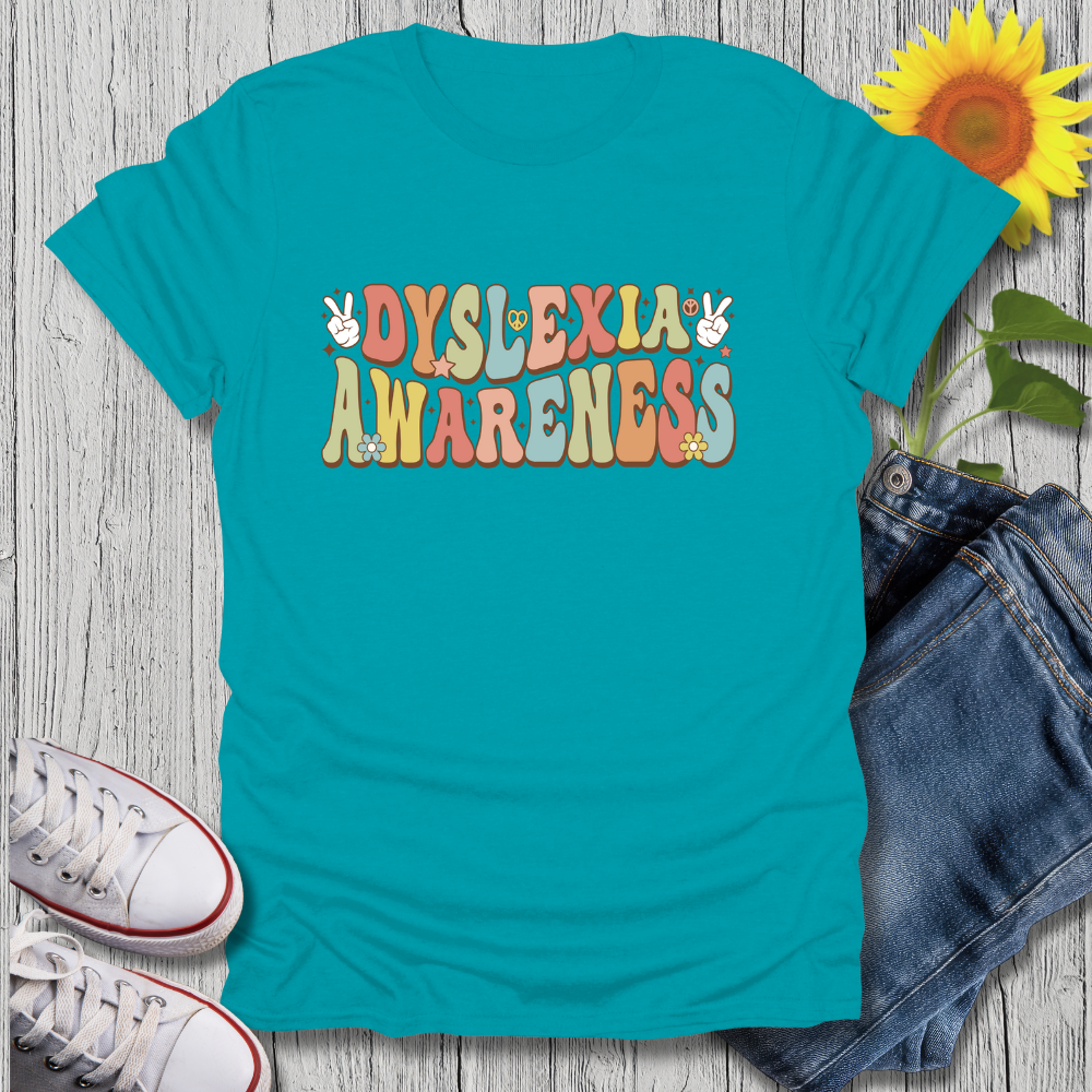 Turquoise t-shirt with 'Dyslexia Awareness' text on a wooden surface with jeans and sneakers.
