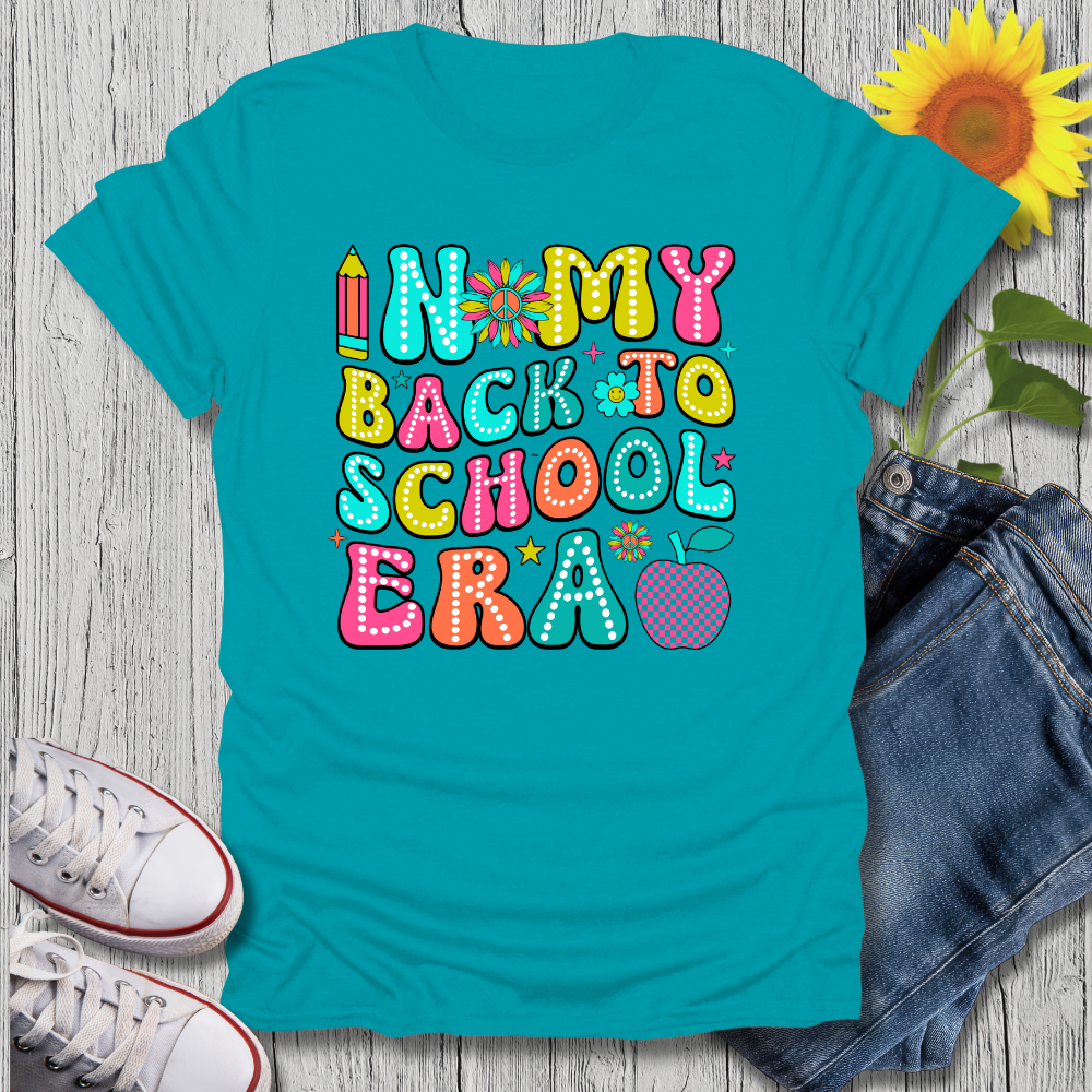 Turquoise t-shirt with colorful 'Back to School' text on a wooden surface with jeans, sneakers, and a sunflower.