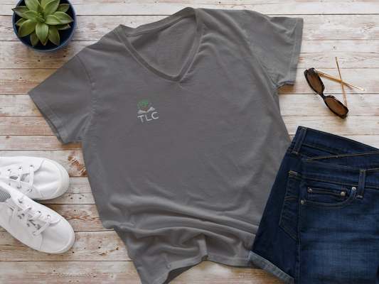 Gray t-shirt with a logo on a wooden surface with jeans, sneakers, and sunglasses.